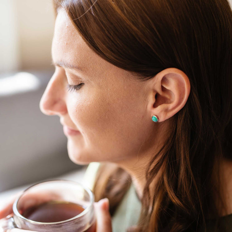 Model wearing hypoallergenic green Opal stud earrings holding  cup of tea