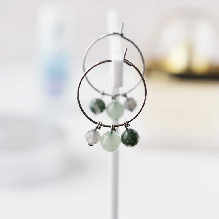 Green gemstone hoop earrings hanging against soft focus background