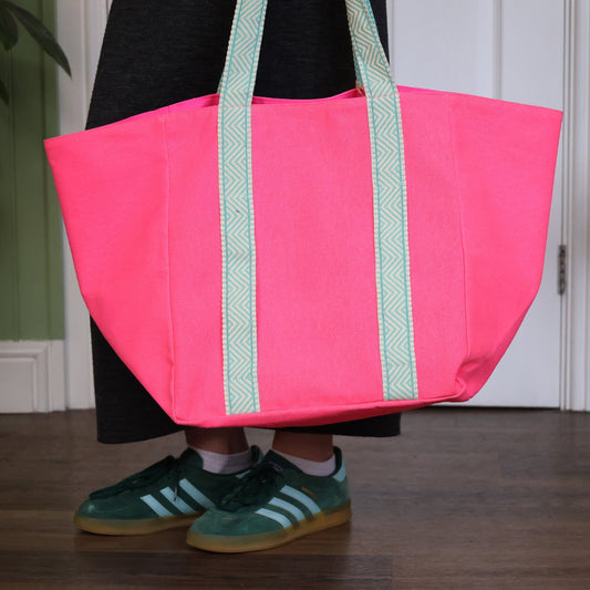 Person holding a pink tote bag with green straps indoors.