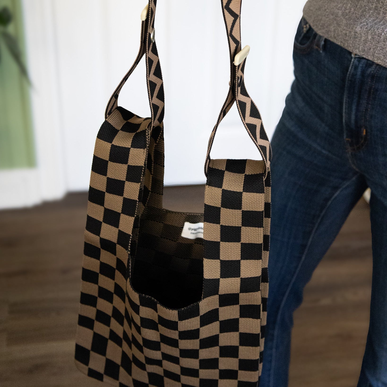 Black and beige checkered bag with zigzag strap held by a person wearing blue jeans.