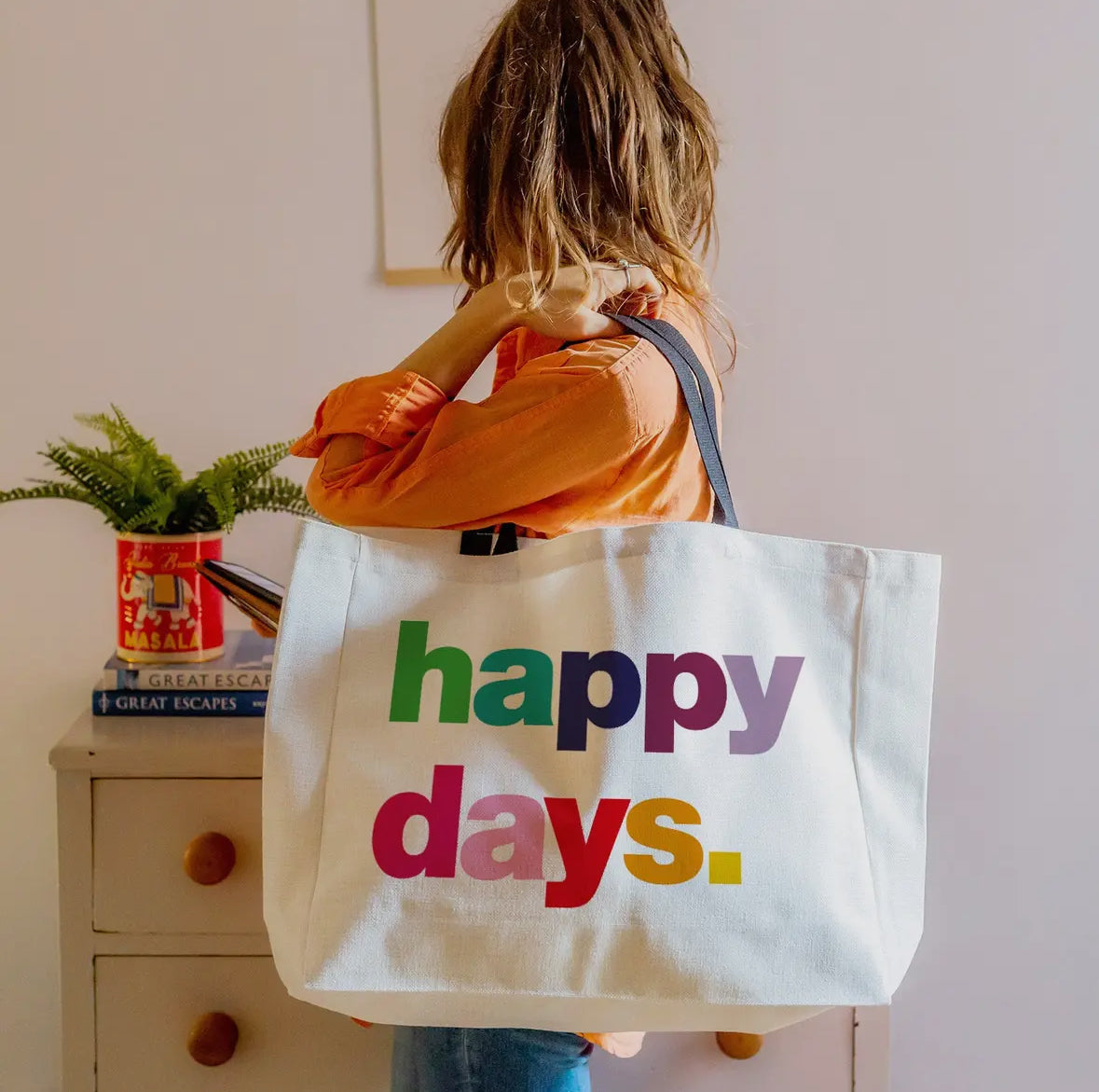 Person holding a tote bag with 'happy days' text in a home setting