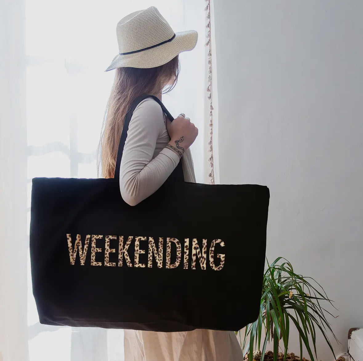 Person holding a black tote bag with 'WEEKNIGHTING' text, wearing a hat indoors.