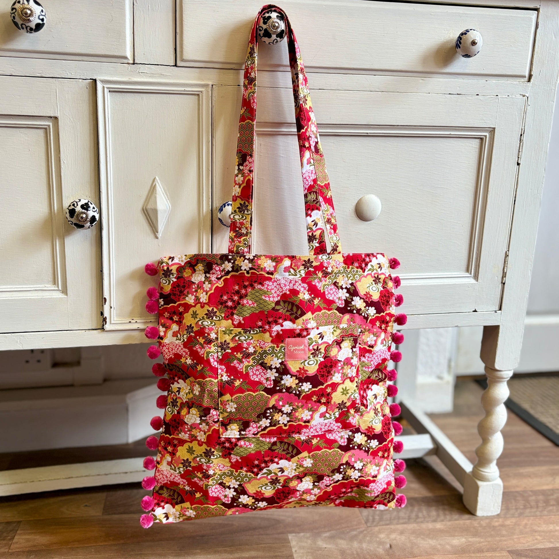 Colorful fabric bag with pom-poms hanging on a white cabinet.