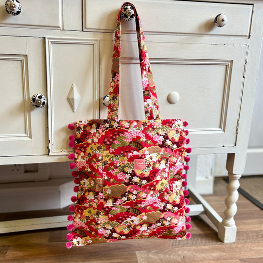 Colorful fabric bag with pom-poms hanging on a white cabinet.