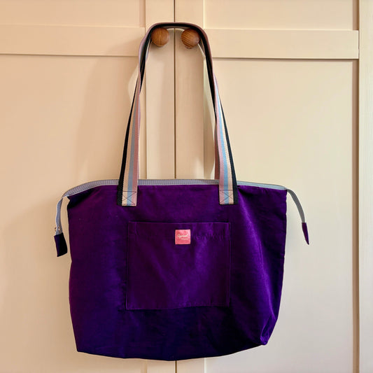 Purple tote bag with a pink tag on a wooden door