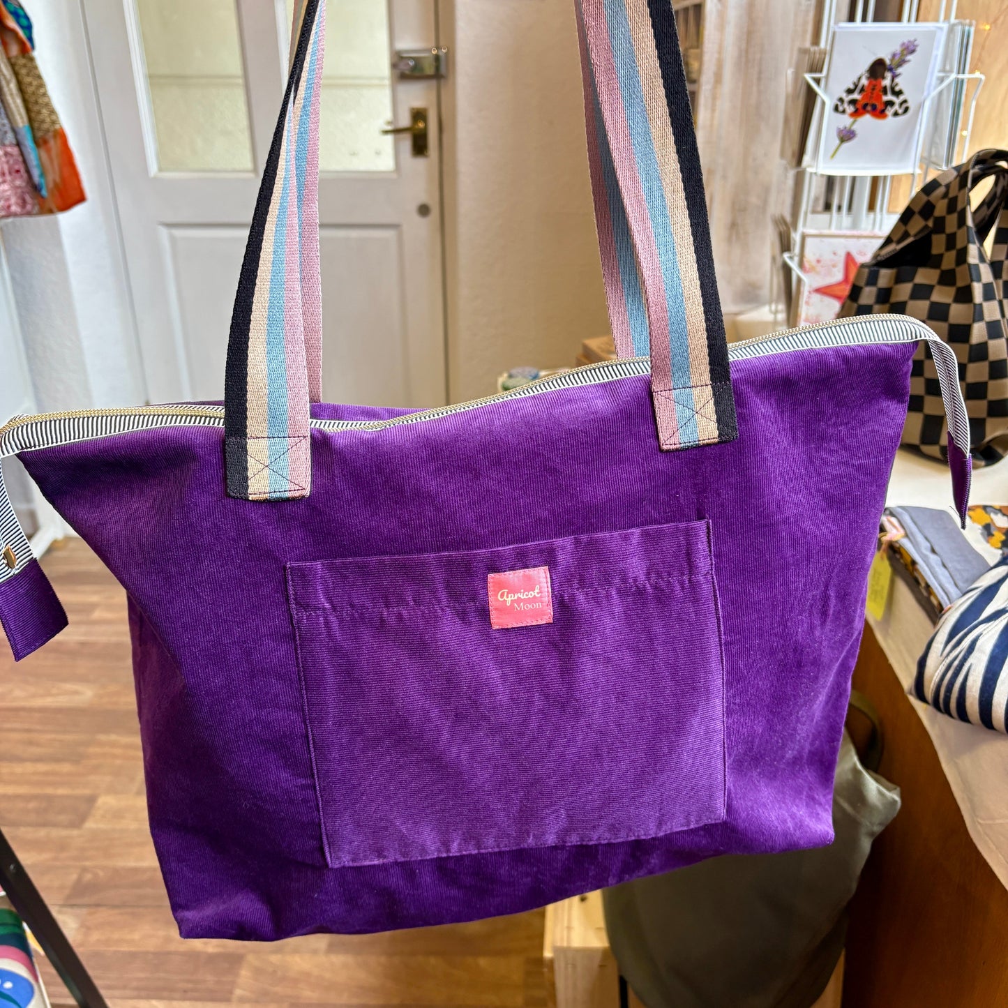 Purple tote bag with rainbow straps in a room setting