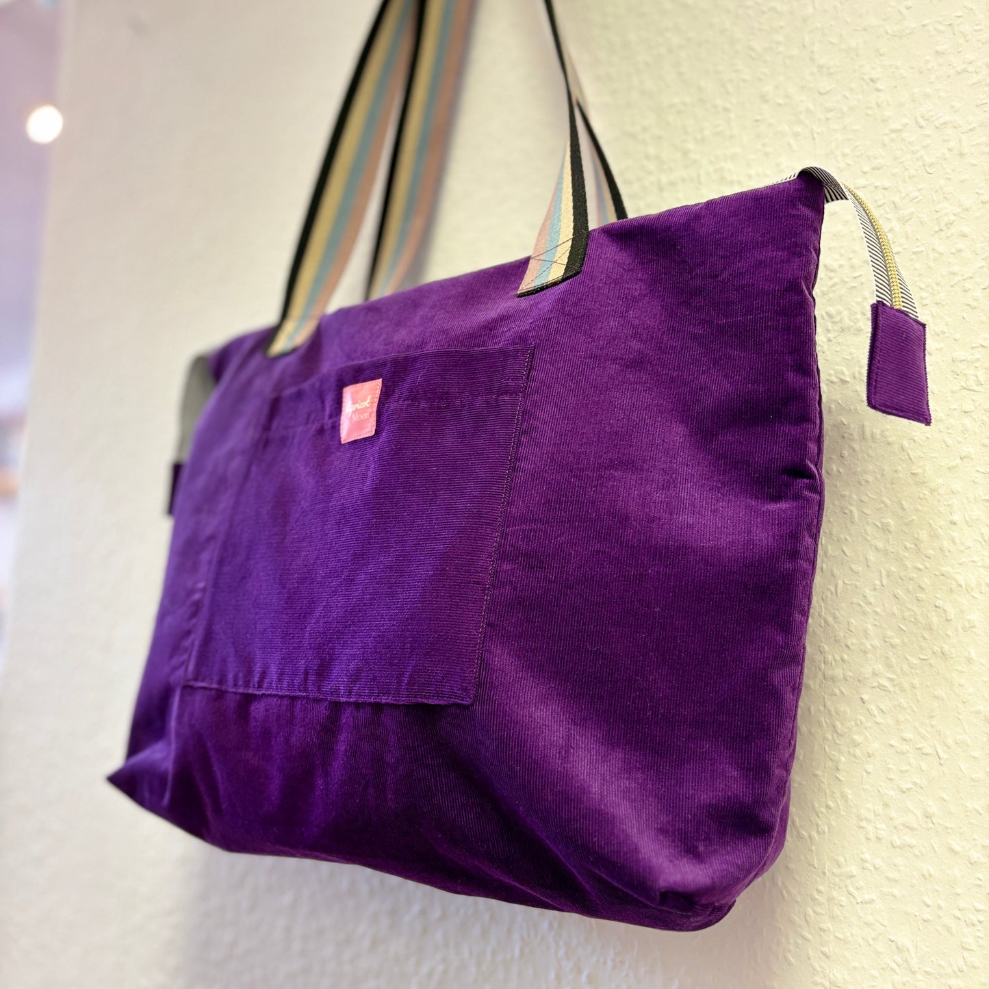 Purple tote bag with striped handles on a white background