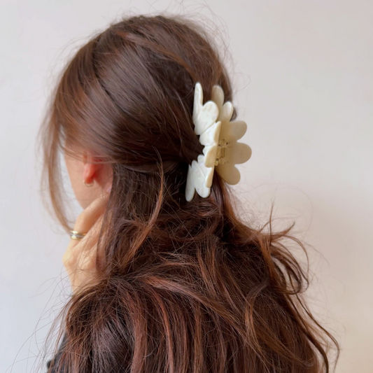 Woman with brown hair wearing a white floral hair clip against a plain background