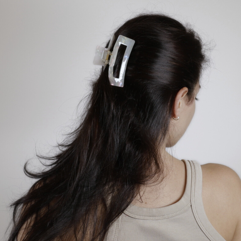 Person with long dark hair wearing a silver hair clip on a plain background