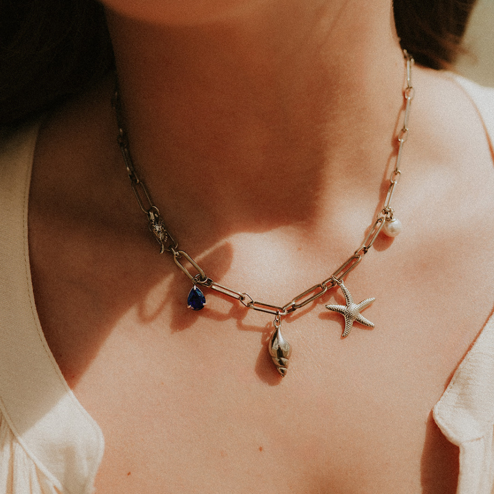 Necklace with starfish, shell, and blue stone pendant on a person wearing a beige top.