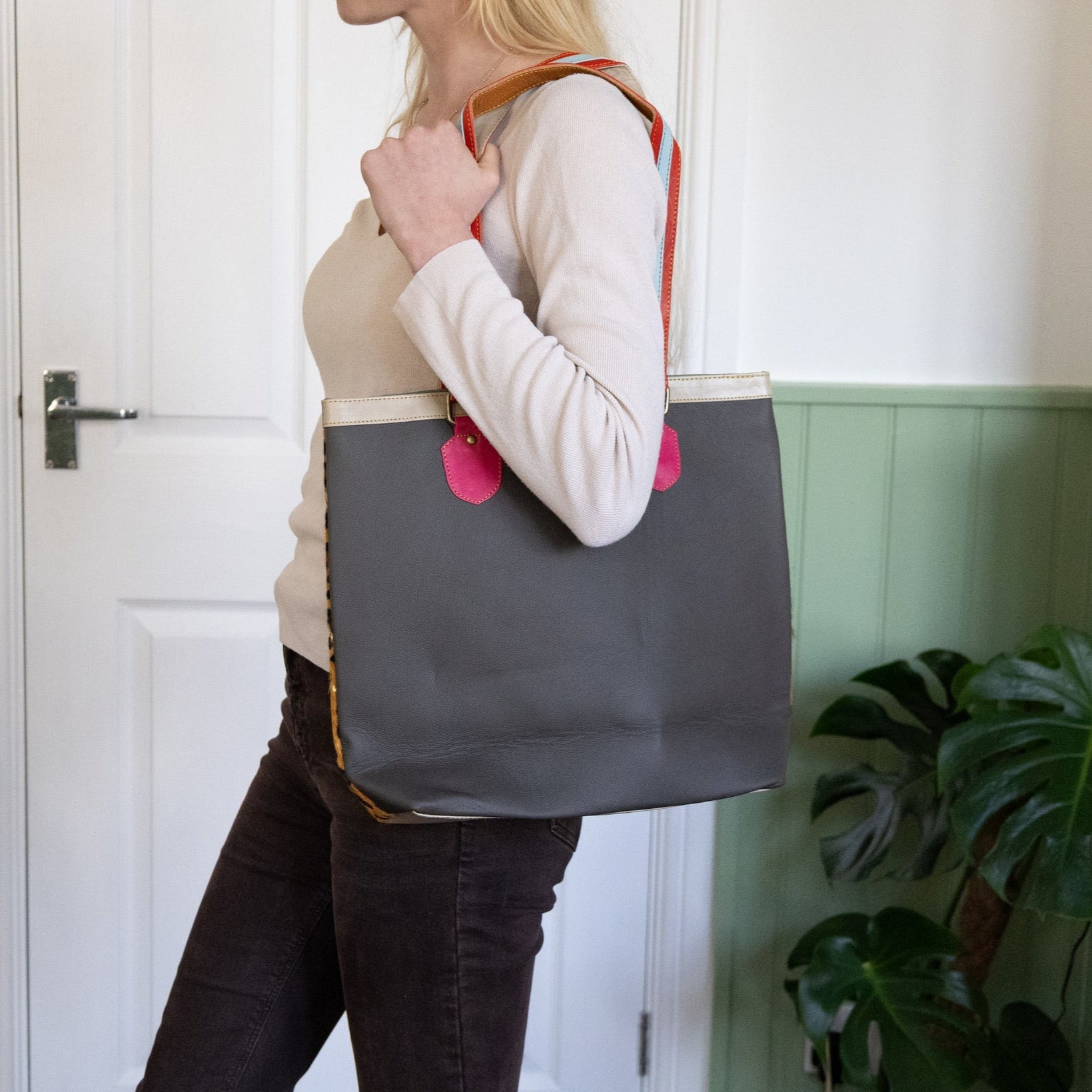 Woman holding a gray tote bag with pink accents indoors.