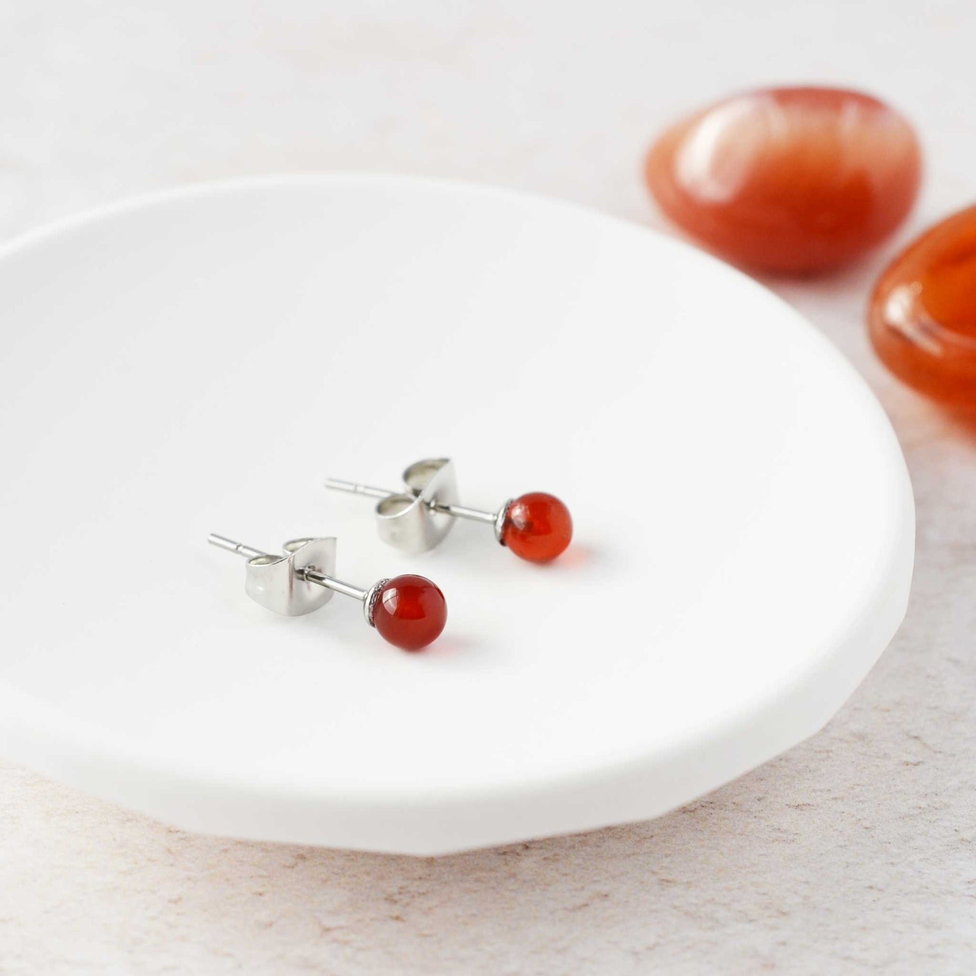 Tiny orange Carnelian stud earrings laying in white trinket dish.
