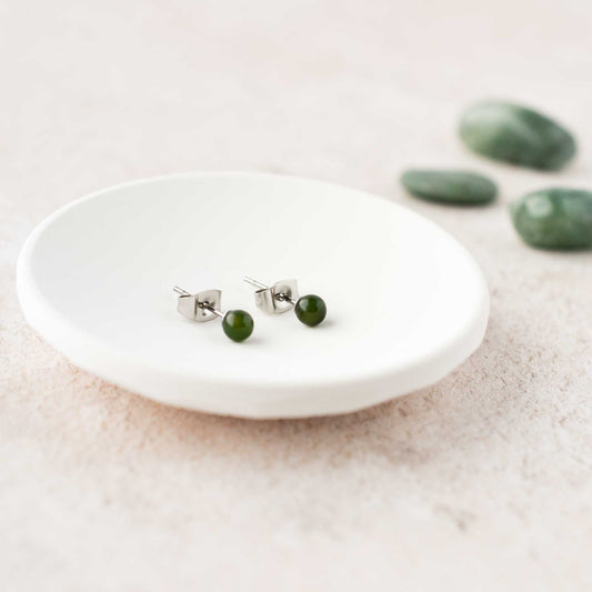 Small dark green Jade gemstone ball stud earrings laying in white trinket dish.