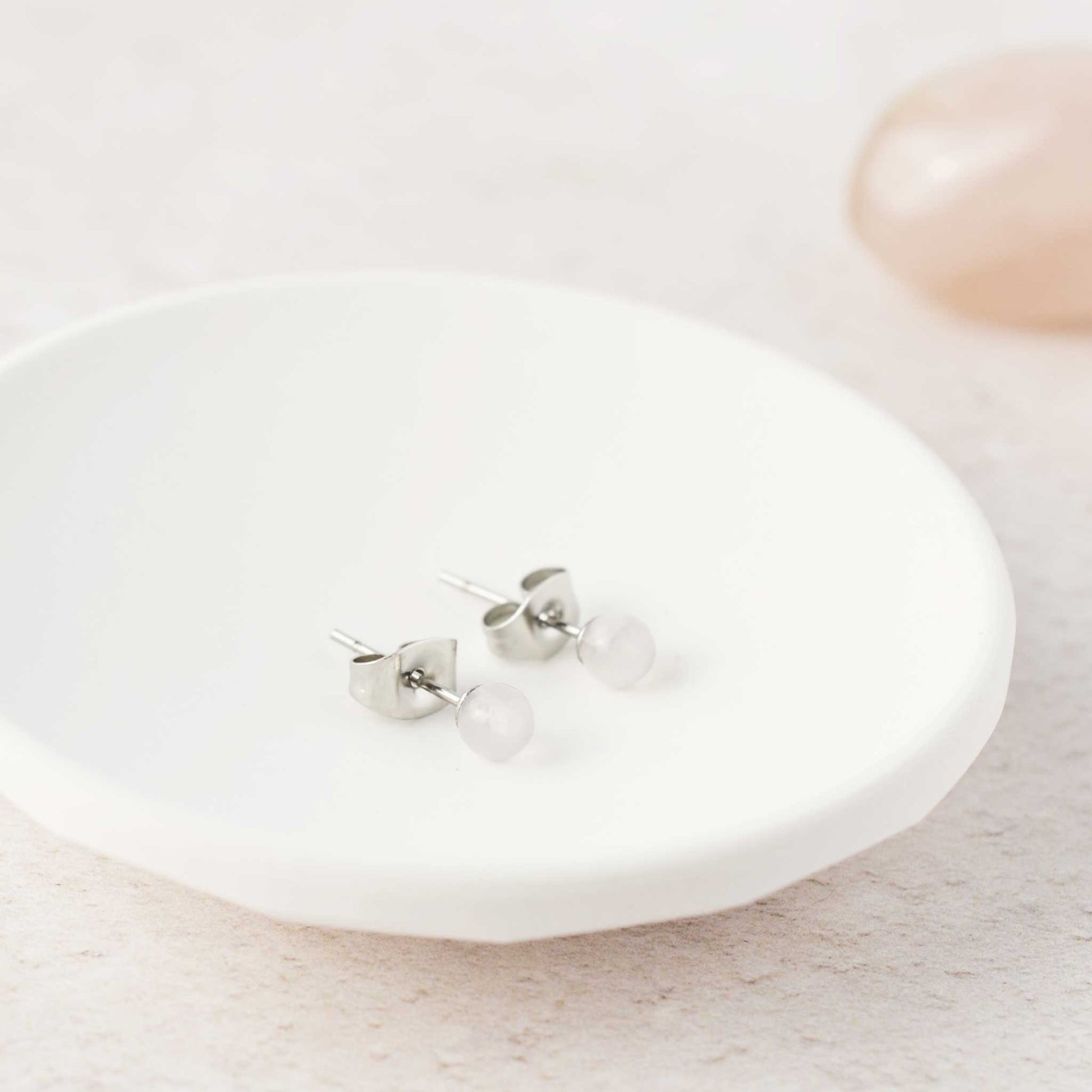 Tiny pale pink Rose Quartz stud earrings laying in white trinket dish.