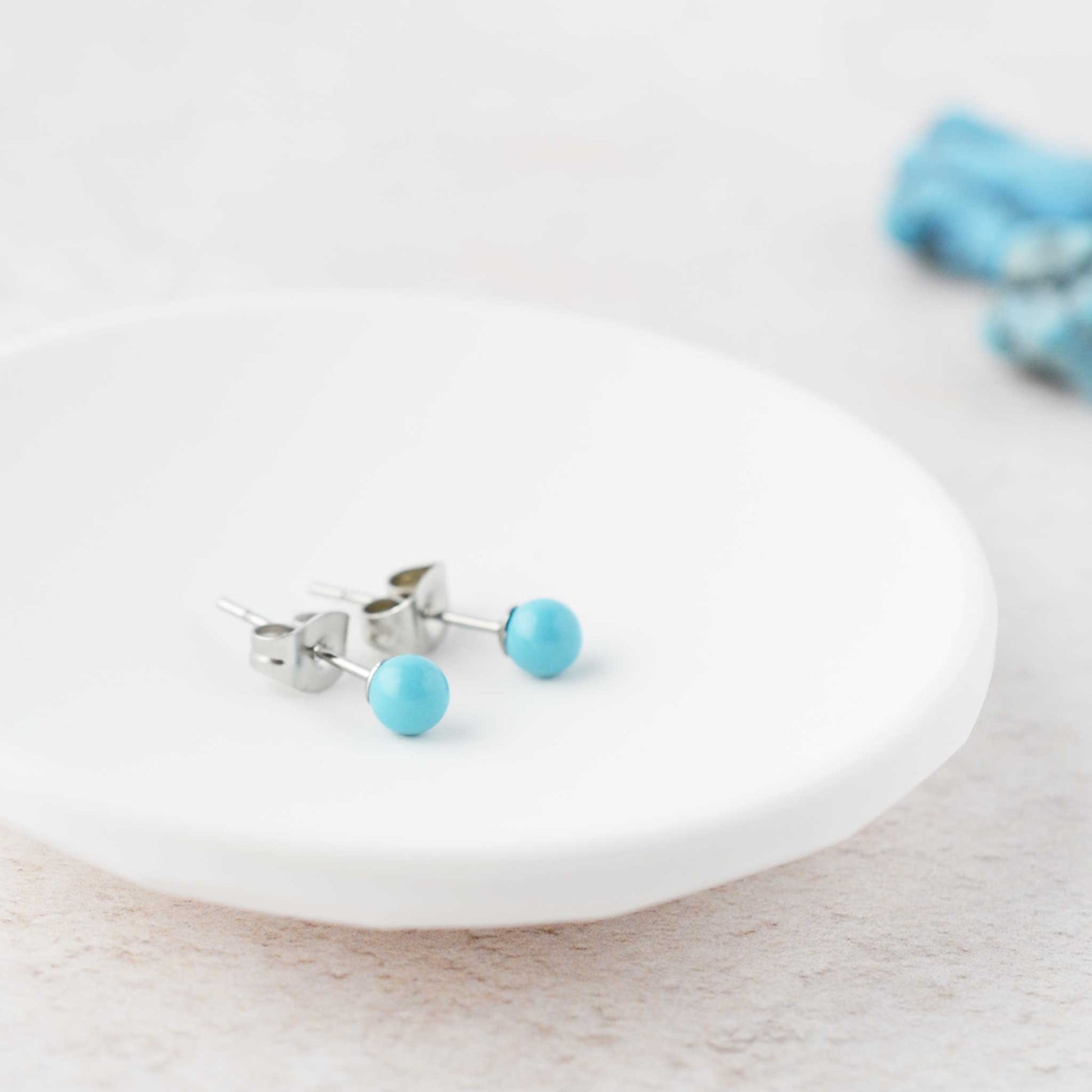 Tiny Turquoise ball stud earrings laying in white trinket dish.