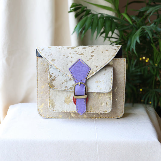 Small beige handbag with a purple strap on a white surface with a plant in the background