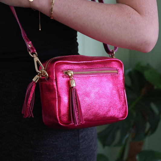 Person holding a pink crossbody bag with gold accents