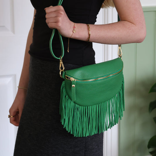 Green fringed handbag held by a person against a neutral background