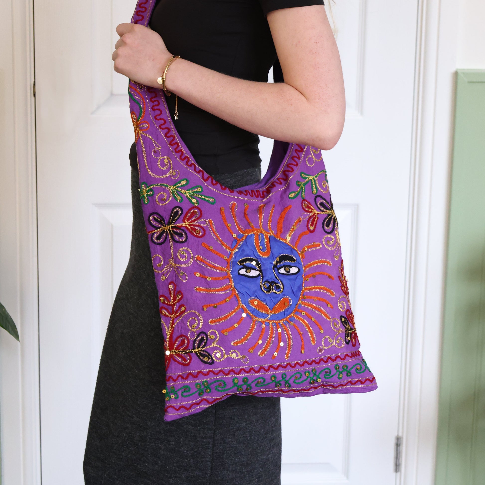 Person holding a colorful embroidered bag with a sun design against a white door background.