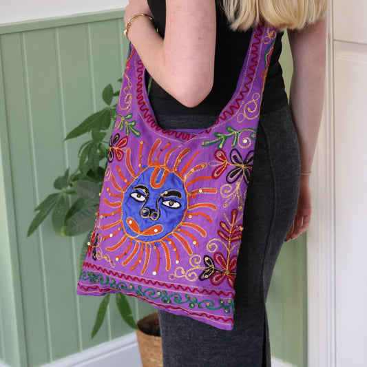 Person holding a colorful embroidered bag with a sun design against a green wall.