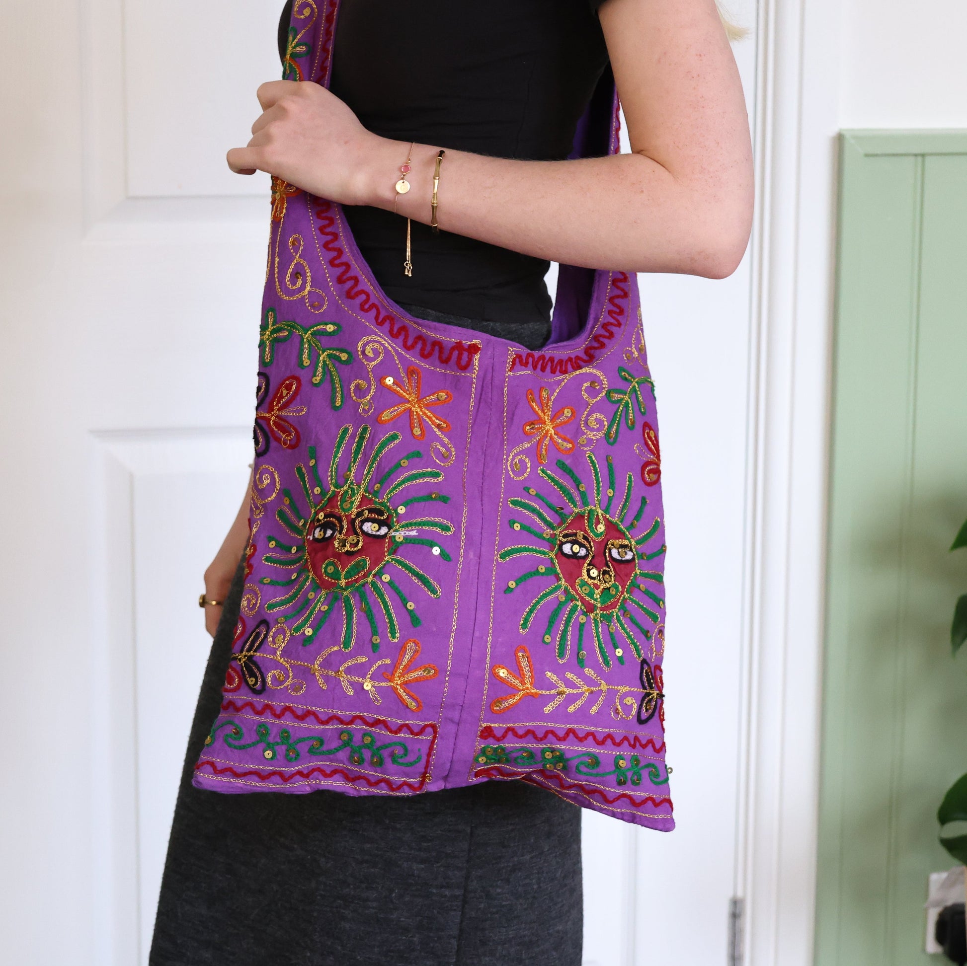 Person holding a colorful embroidered bag with a white door and green plant in the background