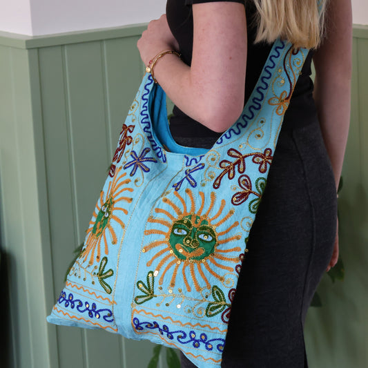 Person holding a blue embroidered bag with sun design against a green wall.