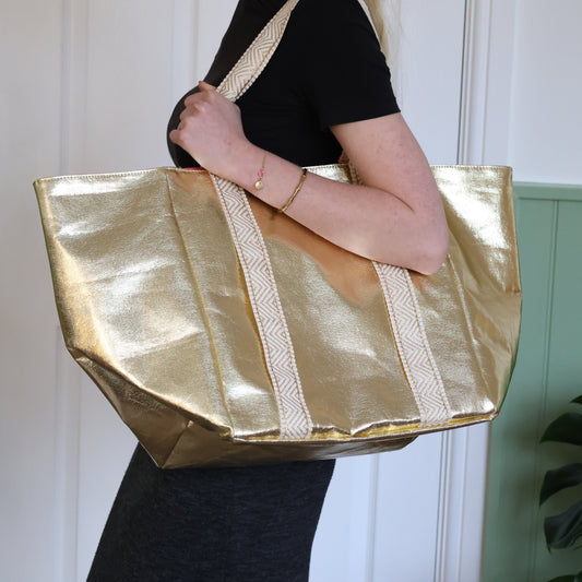 Person holding a gold tote bag with a white wall background