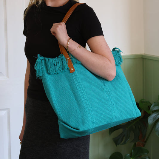 Person holding a teal bag with fringes indoors