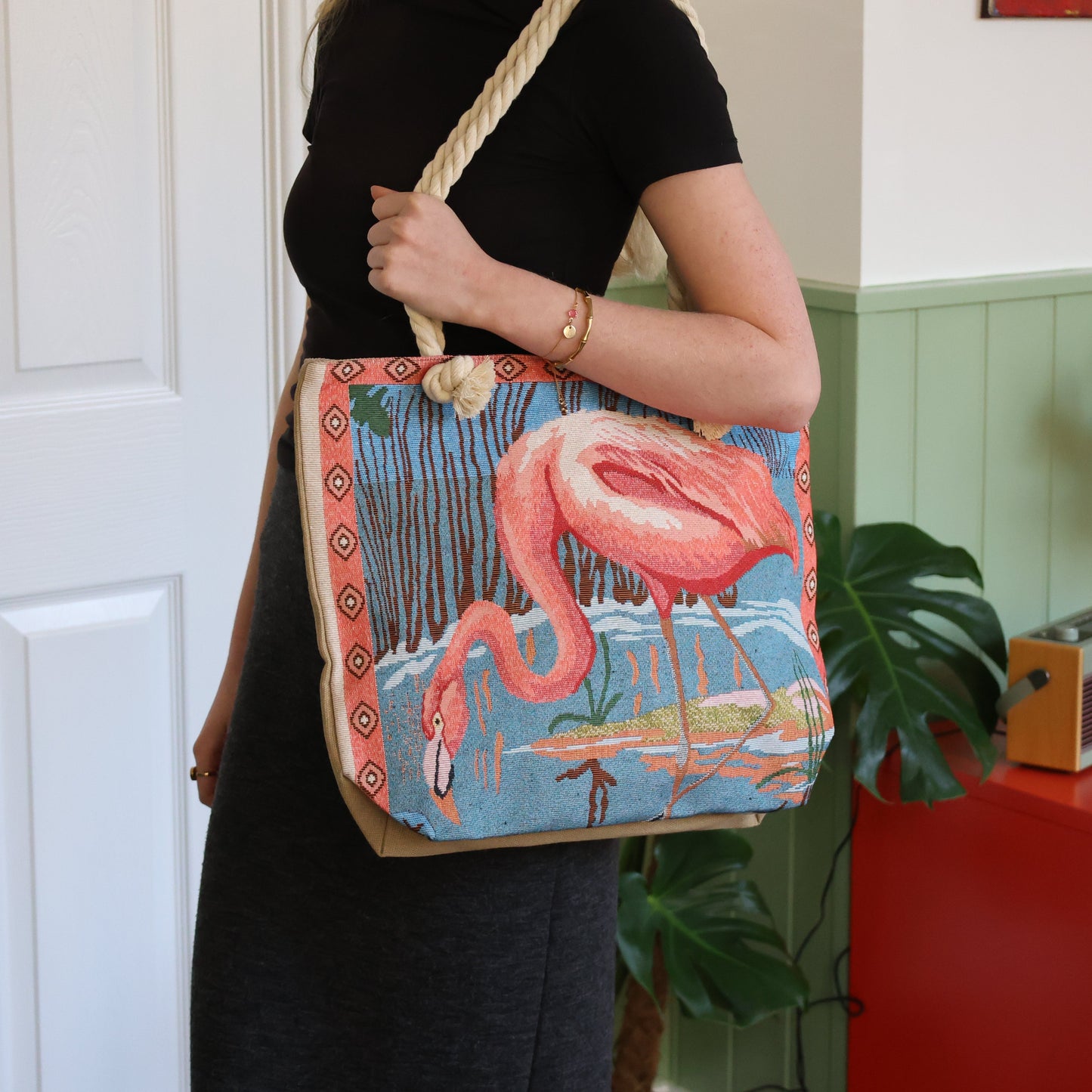 Person holding a tote bag with a flamingo design in a home setting