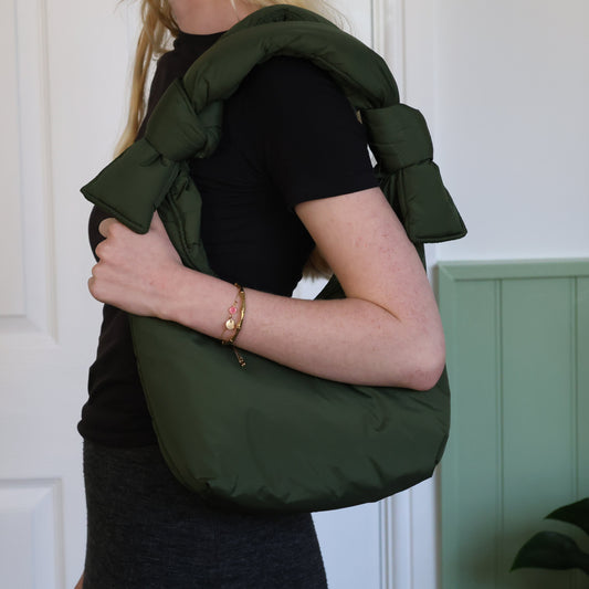 Person wearing a green shoulder bag against a white wall.