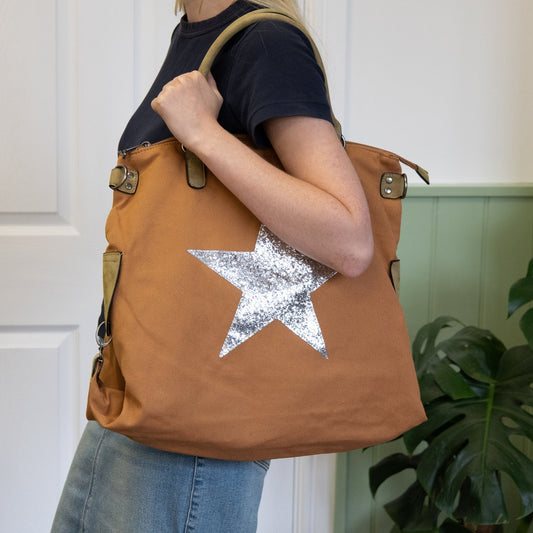Person holding a brown tote bag with a silver star design, standing indoors.