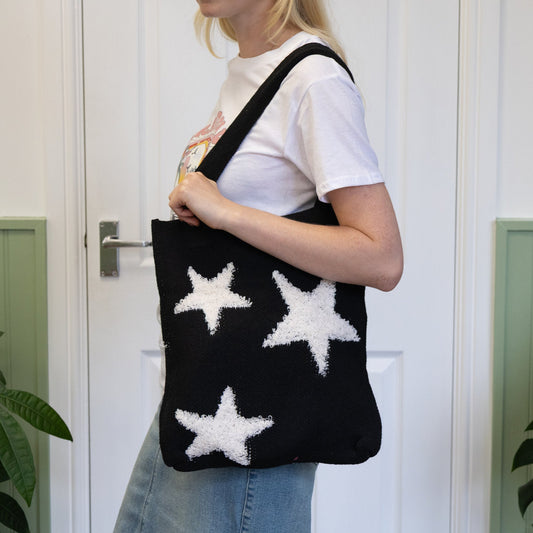 Person holding a black tote bag with white star patterns against a white door background
