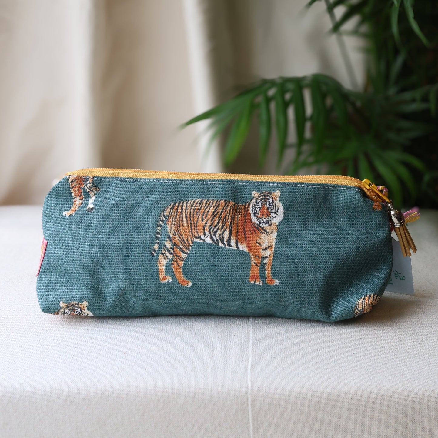 Teal pouch with tiger design on a white surface with a plant in the background