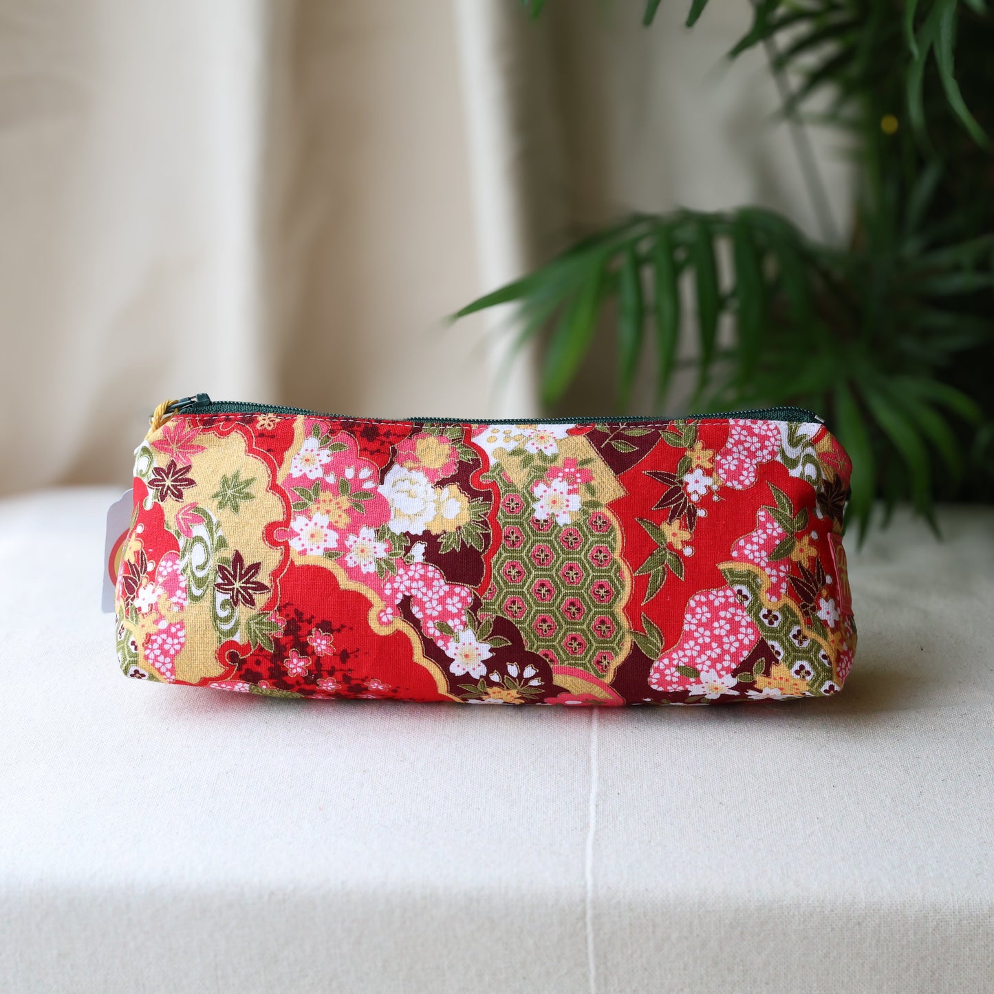 Floral patterned pouch on a white surface with a plant in the background