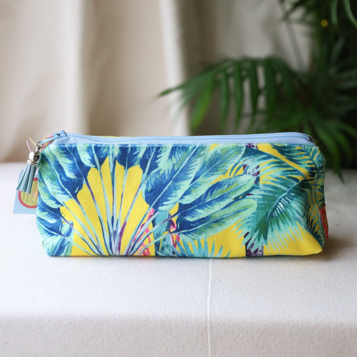Tropical leaf patterned pouch on a white surface with a plant in the background