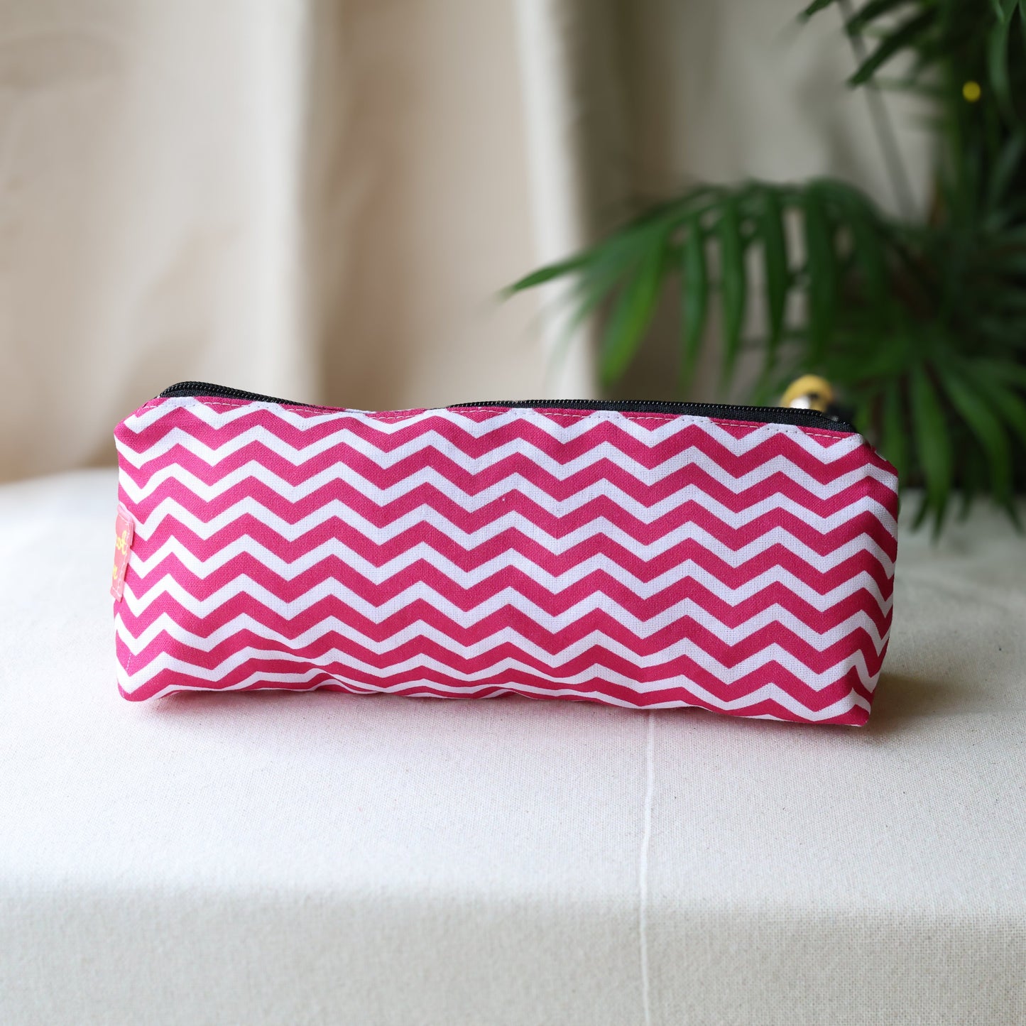 Pink and white chevron patterned pouch on a light surface with a plant in the background