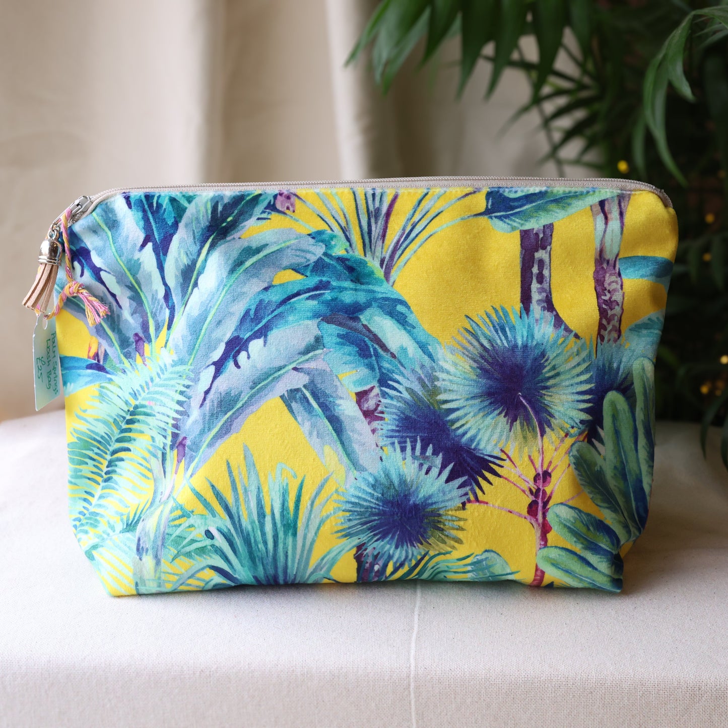 Colorful palm leaf patterned pouch on a white surface with a plant in the background