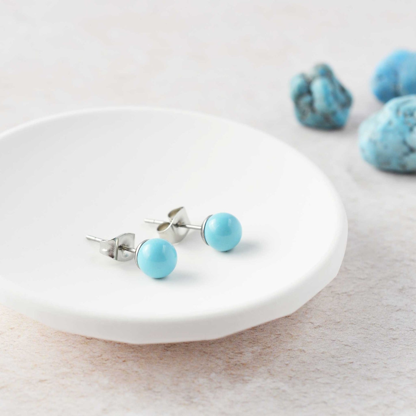 Turquoise gemstone ball stud earrings laying in white trinket dish.