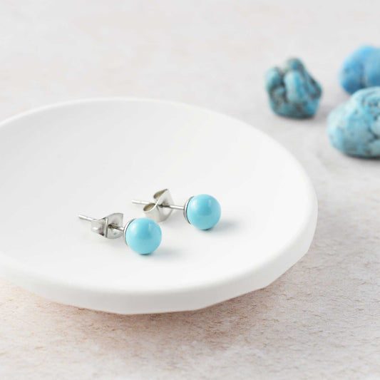 Turquoise gemstone ball stud earrings laying in white trinket dish.