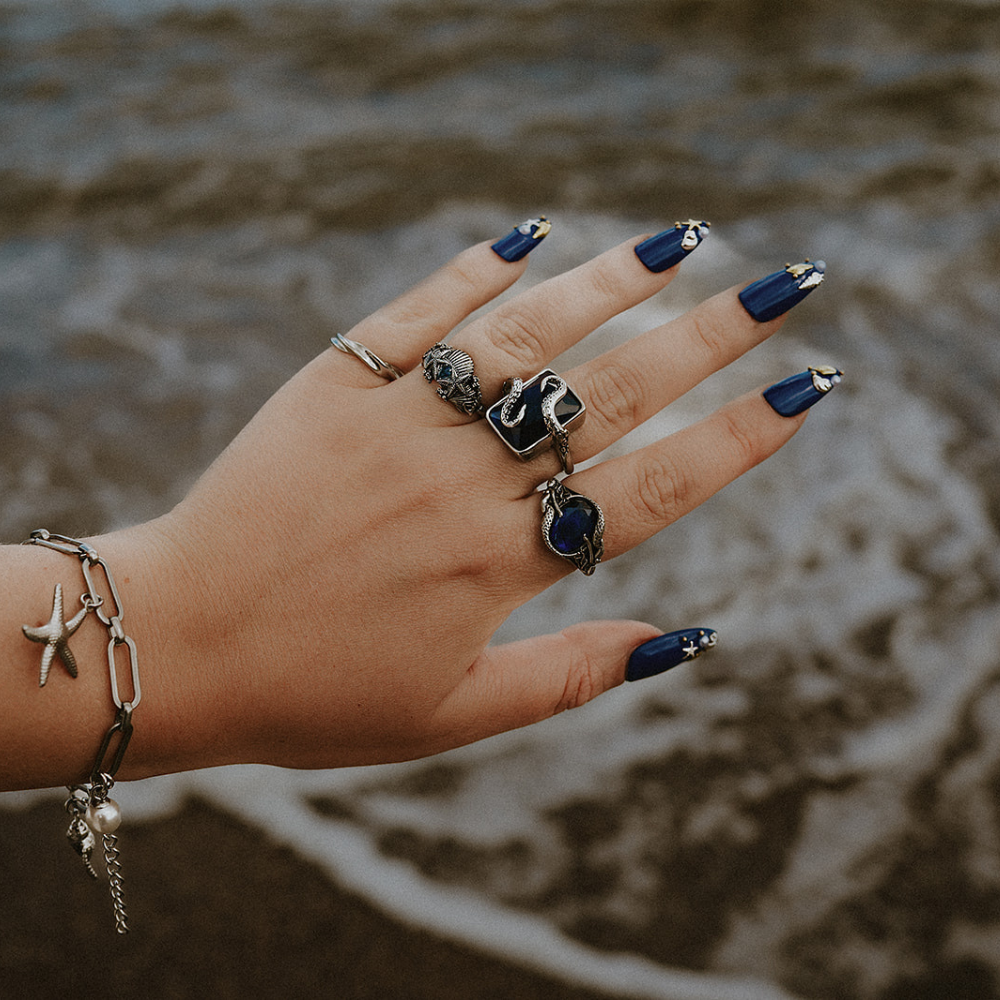 Hand with multiple rings and bracelets against a blurred natural background