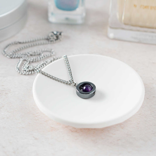 Amethyst spinner necklace laying on white trinket dish.