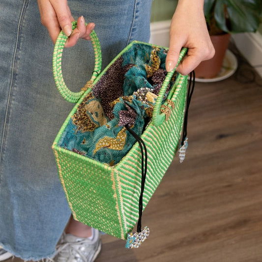 Person holding a green handbag with floral pattern and decorative elements.