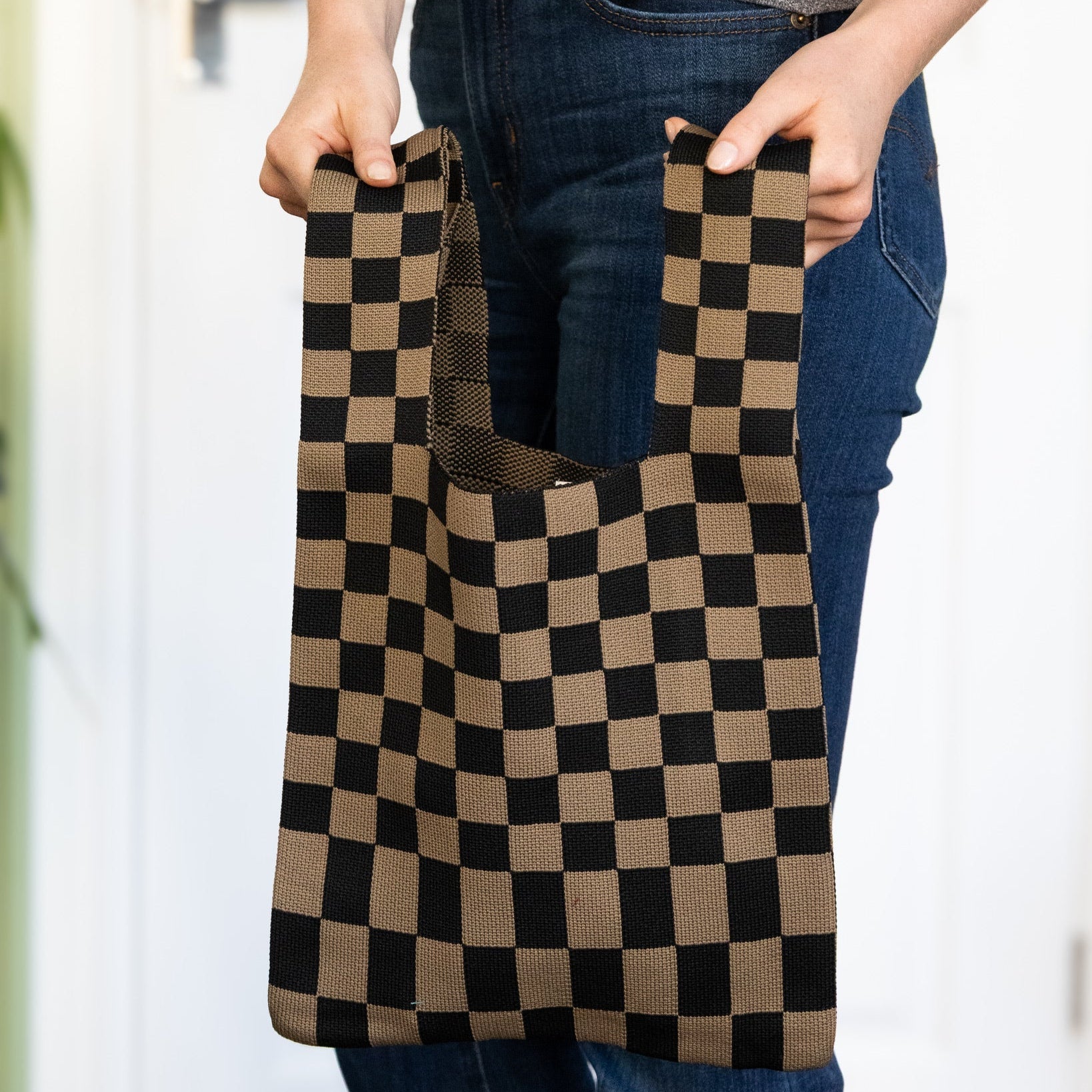 Person holding a checkered brown and black reusable bag.