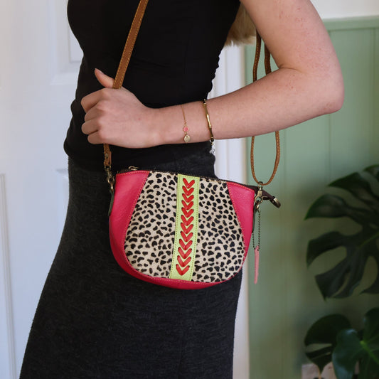 Person holding a pink crossbody bag with leopard print and tribal patterns.