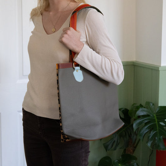 Person holding a gray tote bag with a colorful strap indoors.