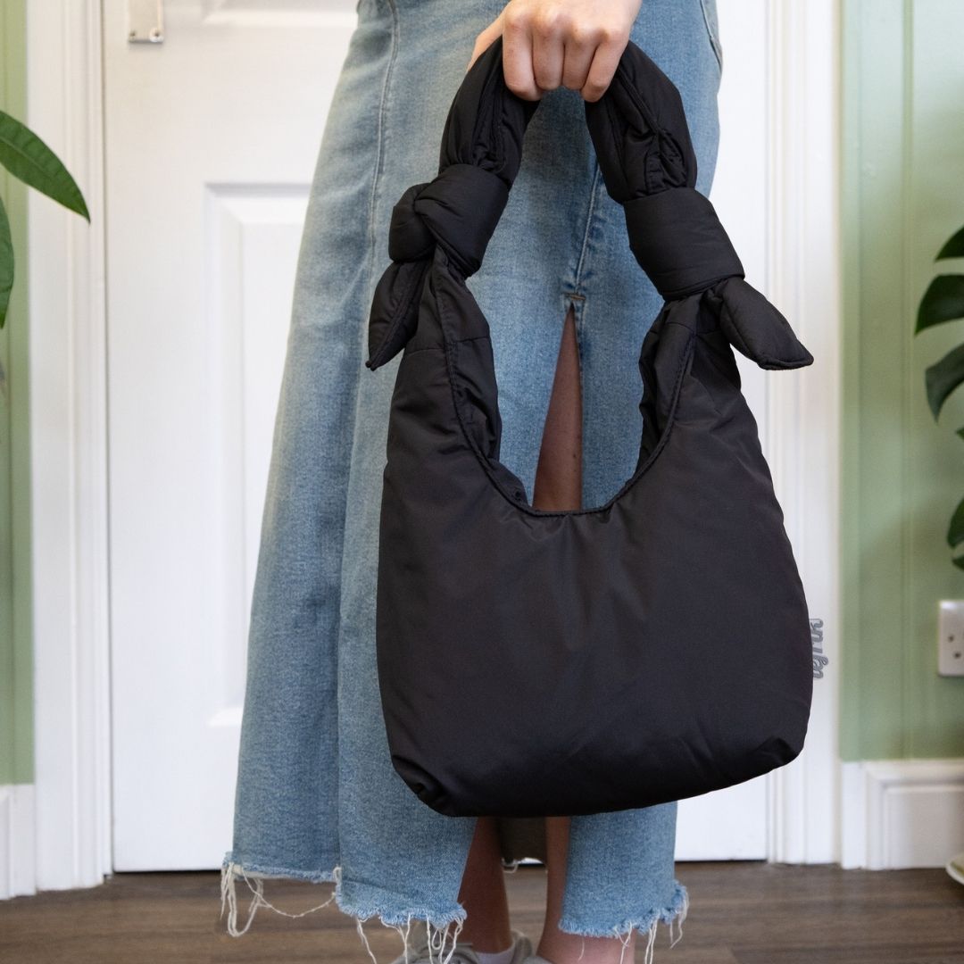 Person holding a black bag with denim accents indoors