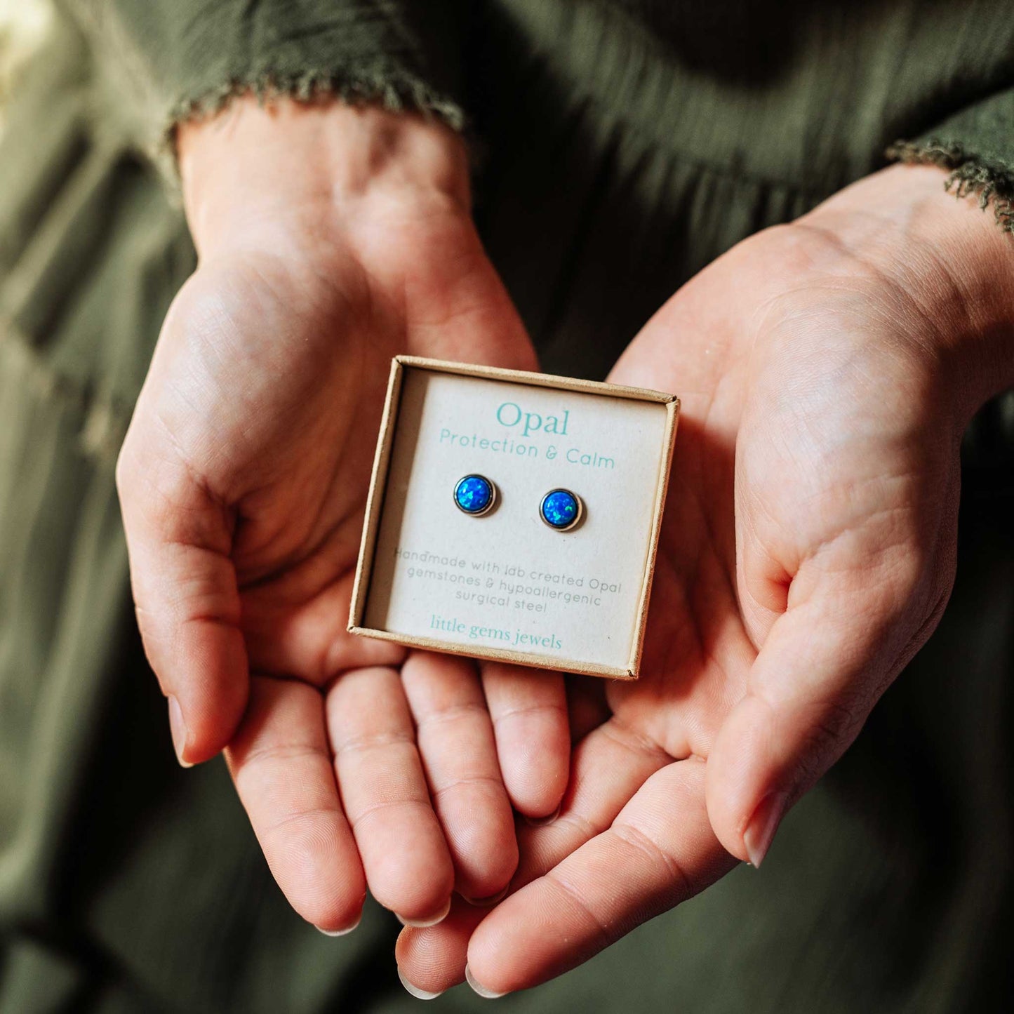 Opal earrings in a box held in hands against a blurred background