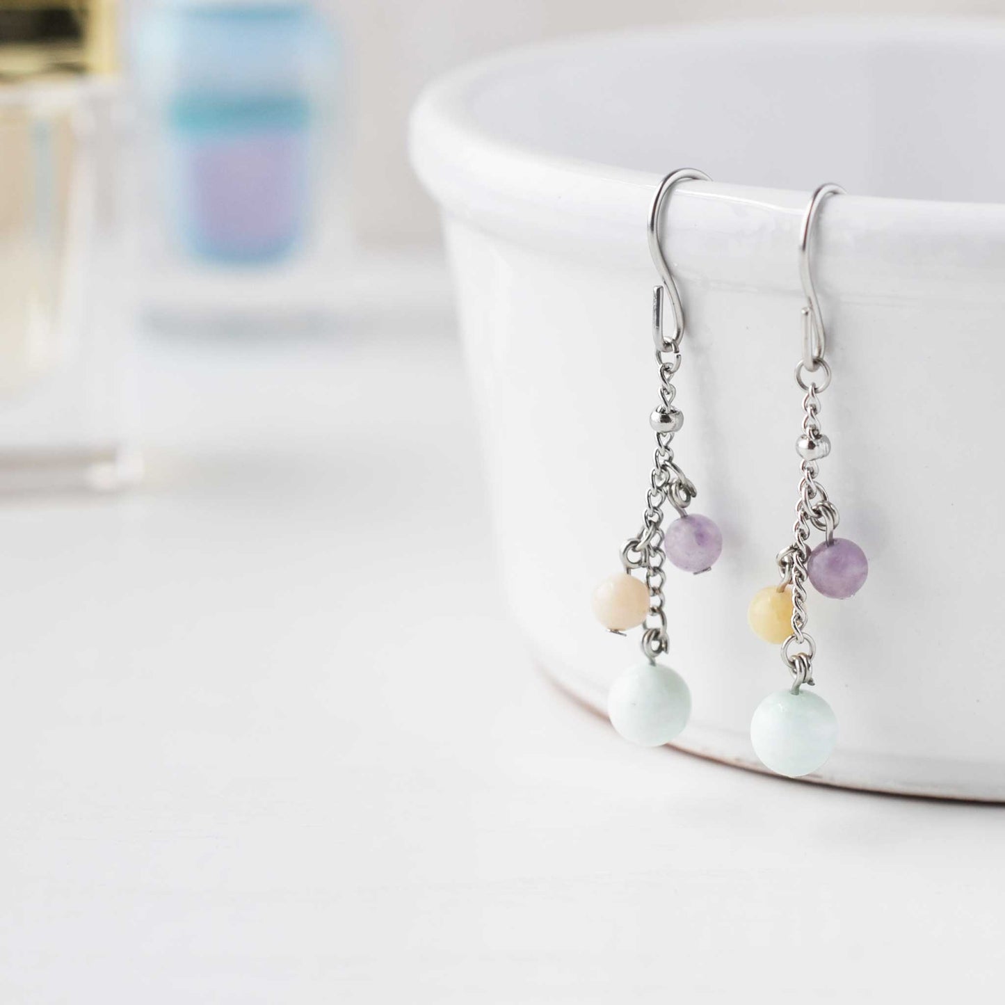 Pastel gemstone drop earrings hanging on white cup against soft focus background