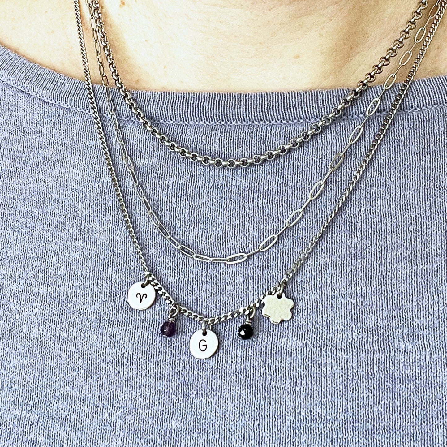 Woman wearing three chains in a layered style with charms hanging on the longest chain.