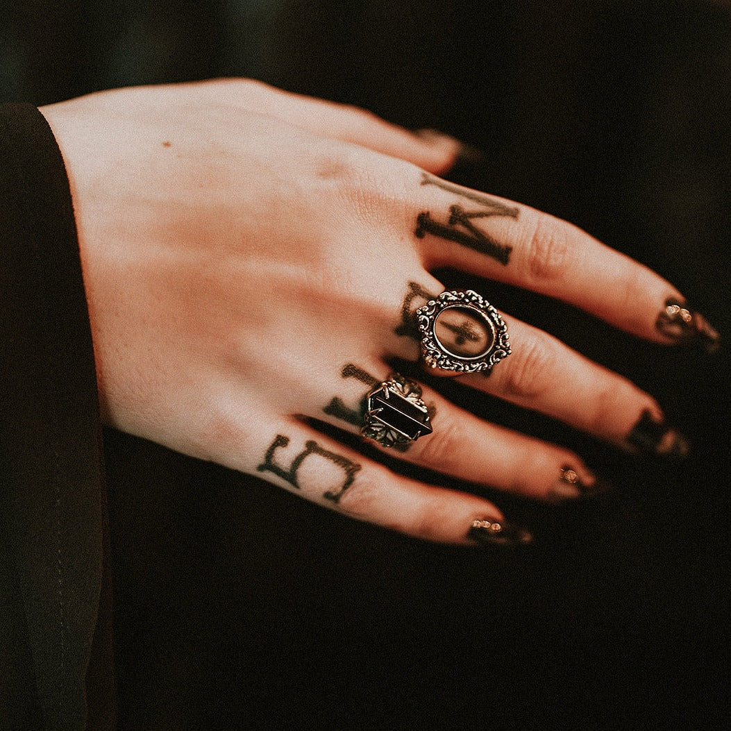 Hand with tattoos and rings on a dark background